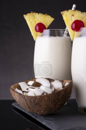 Photo for Two glasses of pina colada cocktail with dark rum, pineapple juice and coconut cream, decorated with pineapple slices and maraschino cherry - Royalty Free Image