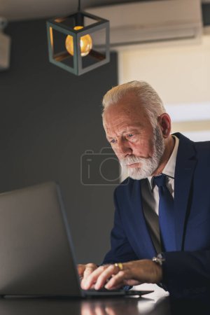 Foto de Hombre de negocios sénior en la oficina moderna que trabaja en un ordenador portátil, pensativo y serio - Imagen libre de derechos