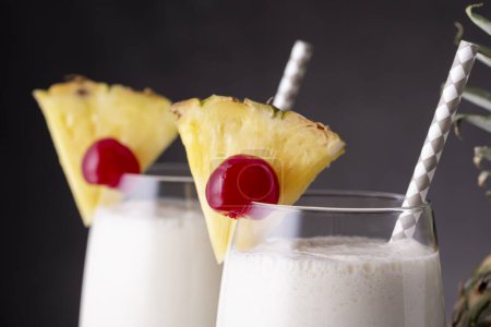 Photo for Detail of two glasses of pina colada cocktail with dark rum, pineapple juice and coconut cream, decorated with pineapple slices and maraschino cherry - Royalty Free Image