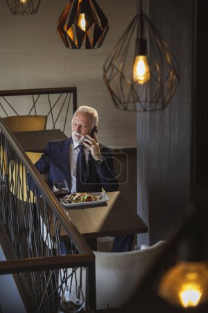 Téléchargez les photos : Homme d'affaires senior prenant une pause, déjeunant dans un restaurant et apeaking au téléphone - en image libre de droit