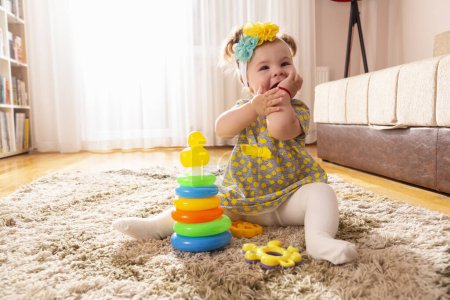 Foto de Hermosa niña jugando con pilas de colores de diferentes círculos de tamaño juguete didáctico y masticar sus manos - Imagen libre de derechos