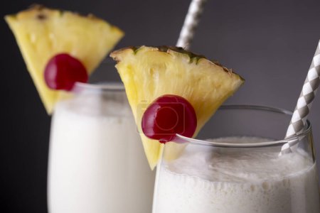 Photo for Detail of two glasses of pina colada cocktail with dark rum, pineapple juice and coconut cream, decorated with pineapple slices and maraschino cherry - Royalty Free Image