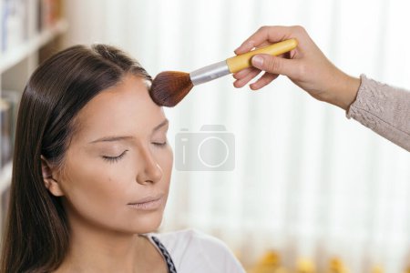 Photo for Make up artist working in a make up studio, applying the highlighters to female client's face - Royalty Free Image