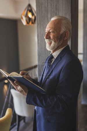 Photo for Senior businessman working, taking notes in a planner, updating his schedule - Royalty Free Image