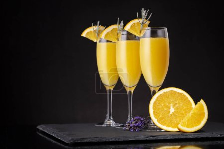 Foto de Cócteles Mimosa en copas de champán con zumo de naranja y vino espumoso decorado con hojas de lavanda y rodajas de naranja. Concéntrate en el vidrio correcto - Imagen libre de derechos