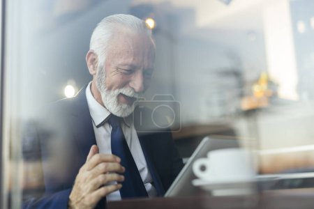 Téléchargez les photos : Homme d'affaires senior dans un restaurant, en utilisant une tablette et en buvant du café - en image libre de droit