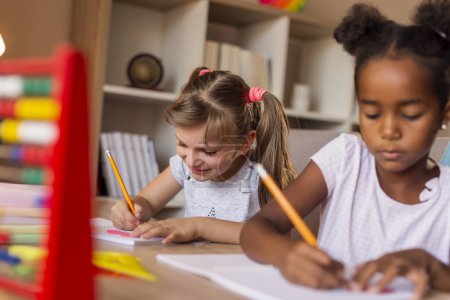 Photo for Two beautiful little girls doing math at home as part of homeschooling due to Covid 19 pandemic social distancing measures; children studying and doing homework at home - Royalty Free Image
