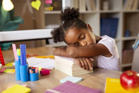 Foto de Hermosa niña cansada de hacer sus deberes, durmiendo en su escritorio, usando un montón de libros como almohada - Imagen libre de derechos