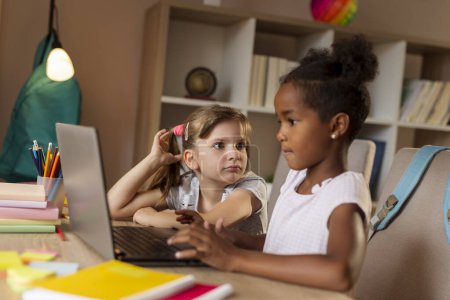 Photo for Two beautiful little girls sitting at a desk, doing homework, finishing a project for school on a laptop computer - Royalty Free Image