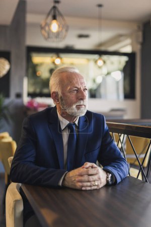 Téléchargez les photos : Portrait d'un cher homme d'affaires âgé assis dans un restaurant moderne d'immeuble de bureaux, prenant une pause café et regardant la distance - en image libre de droit