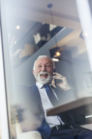 Foto de Hombre de negocios sénior sentado en una mesa de restaurante, teniendo una conversación telefónica - Imagen libre de derechos