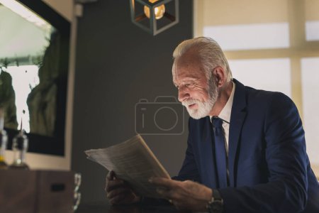 Téléchargez les photos : Homme d'affaires senior debout à côté d'un comptoir dans un restaurant, lisant un journal - en image libre de droit