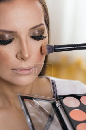 Photo for Make up artist working in a make up studio, applying blush to female client's cheeks - Royalty Free Image
