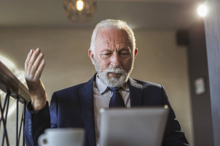 Téléchargez les photos : Homme d'affaires senior dans un restaurant, travaillant sur une tablette informatique, en colère et mécontent - en image libre de droit