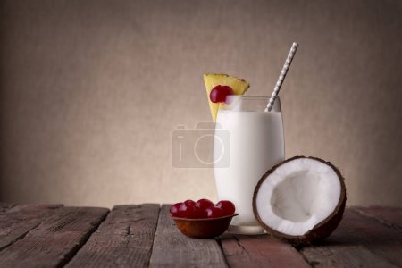 Photo for Pina colada cocktail with dark rum, pineapple juice and coconut cream, decorated with pineapple slices and maraschino cherry on rustic wooden table - Royalty Free Image
