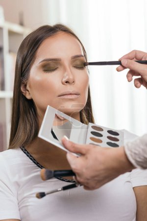 Téléchargez les photos : Maquilleuse travaillant dans un atelier de maquillage, ombrageant les paupières de la cliente - en image libre de droit