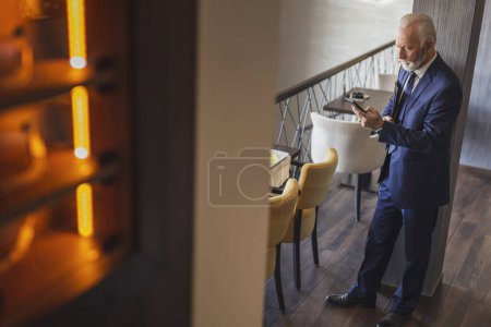 Foto de Hombre de negocios senior parado en un moderno edificio de oficinas, yendo a su lugar de trabajo y escribiendo un mensaje de texto - Imagen libre de derechos
