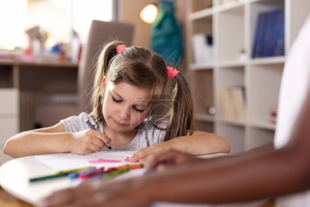 Téléchargez les photos : Deux petites filles assises sur le sol d'une salle de jeux, dessinant avec des crayons, finissant leur projet artistique pour l'école - en image libre de droit