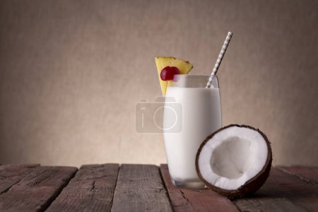 Photo for Glass of pina colada cocktail with dark rum, pineapple juice and coconut cream, decorated with pineapple slices and maraschino cherry on rustic wooden table - Royalty Free Image