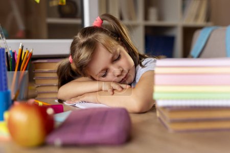 Photo for Beautiful little girl sitting at her desk, tired of doing homework, sleeping next to a pile of books - Royalty Free Image