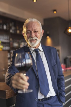 Téléchargez les photos : Homme d'affaires senior debout à côté d'un comptoir dans un restaurant, porter un toast après avoir fait une affaire réussie - en image libre de droit