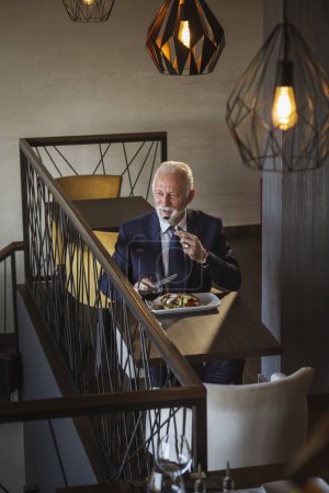 Photo for Senior businessman taking a break, having lunch in a restaurant - Royalty Free Image