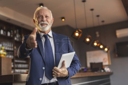 Photo for Senior businessman standing next to a modern office building restaurant counter, waiting for a meeting and offering hand for handshake to colleague - Royalty Free Image
