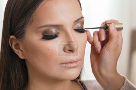 Téléchargez les photos : Maquilleuse travaillant dans un atelier de maquillage, appliquant un eye-liner sur les paupières d'une cliente - en image libre de droit