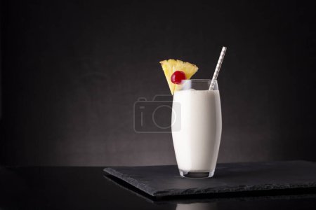 Photo for Glass of pina colada cocktail with dark rum, pineapple juice and coconut cream, decorated with pineapple slices and maraschino cherry - Royalty Free Image