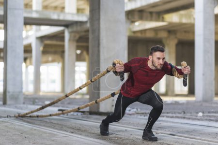 Foto de Atlético, hombre musculoso haciendo un entrenamiento funcional de cuerdas de batalla, tirando de las cuerdas, ejercitando la fuerza - Imagen libre de derechos