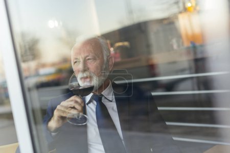 Téléchargez les photos : Portrait d'un homme d'affaires âgé assis à une table de restaurant, buvant du vin - en image libre de droit