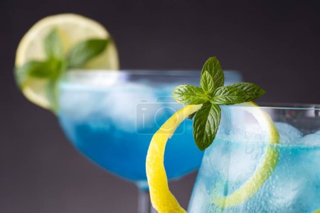 Téléchargez les photos : Détail de deux cocktails lagon bleu avec liqueur de curaçao bleu, vodka, jus de citron et soda, décoré de tranches de citron et de feuilles de menthe - en image libre de droit