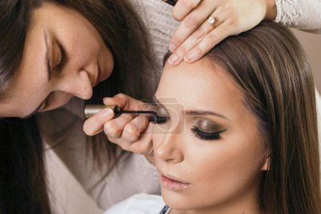 Téléchargez les photos : Artiste maquilleuse travaillant dans un studio de maquillage, mettant de l'eye-liner sur les paupières d'une cliente - en image libre de droit