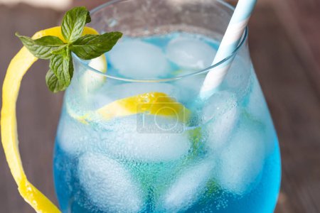 Téléchargez les photos : Détail d'un verre de cocktail lagon bleu avec liqueur de curaçao bleu, vodka, jus de citron et soda, décoré de tranches de citron et de feuilles de menthe - en image libre de droit