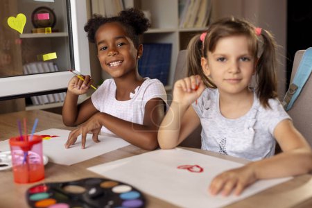 Téléchargez les photos : Deux petites filles assises à un bureau, peignant avec des aquarelles et s'amusant. Concentrez-vous sur la fille à gauche - en image libre de droit