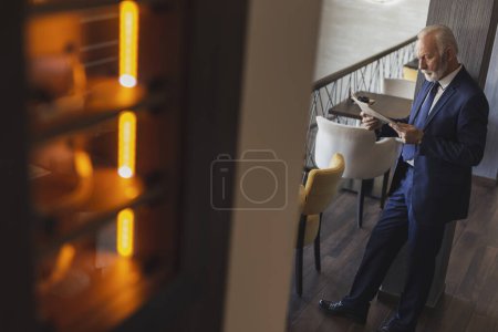 Foto de Senior business man standing in a modern office building restaurante, reading newspaper - Imagen libre de derechos