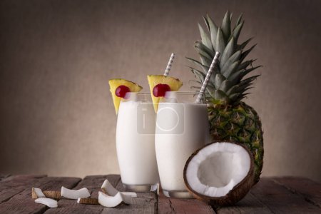 Photo for Two glasses of pina colada cocktail with dark rum, pineapple juice and coconut cream, decorated with pineapple slices and maraschino cherry on rustic wooden table - Royalty Free Image