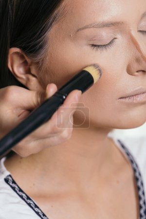 Foto de Maquillaje artista aplicando base de polvo de cara líquida a la cara de un cliente femenino y mezclando contornos - Imagen libre de derechos