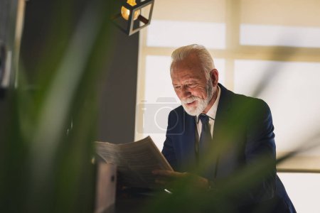 Téléchargez les photos : Homme d'affaires senior debout à côté d'un comptoir dans un café, lisant un journal - en image libre de droit
