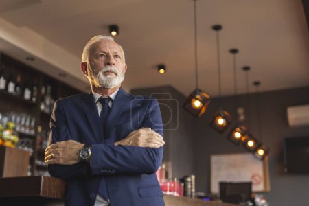 Photo for Portrait of a senior businessman standing by the moden office building restaurant counter with hands crossed on chest, looking at distance - Royalty Free Image