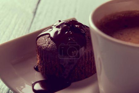 Photo for Cup of coffee on a plate next to a chocolate crunches muffin on a wooden table, top view - Royalty Free Image