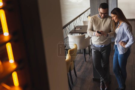 Young couple in love on a date, standing in a restaurant, using a smart phone