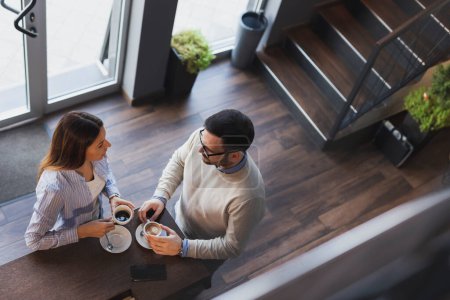 Vista de ángulo alto de una joven pareja enamorada en una cita, de pie junto a un mostrador de restaurante, tomando café y teniendo una conversación