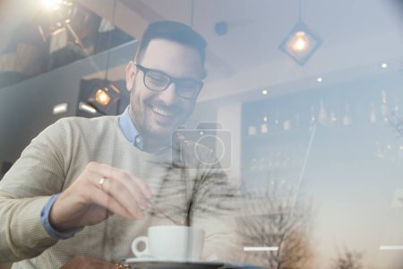 Foto de Retrato de un hombre freelancer sentado en la mesa de un restaurante, tomando café y trabajando en una computadora portátil - Imagen libre de derechos
