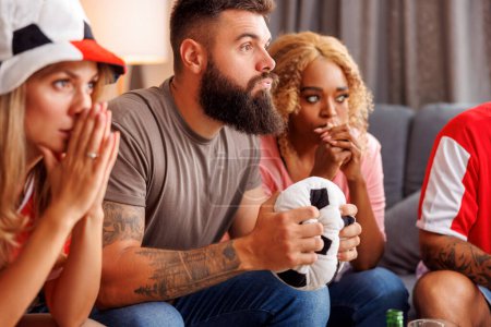 Photo for Group of friends watching football world championship game on TV at home, cheering, eating popcorn and drinking beer - Royalty Free Image