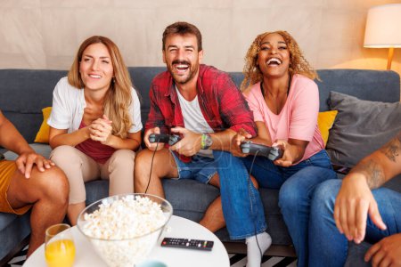 Foto de Grupo de jóvenes amigos alegres que se divierten jugando videojuegos mientras pasan tiempo libre juntos en casa - Imagen libre de derechos