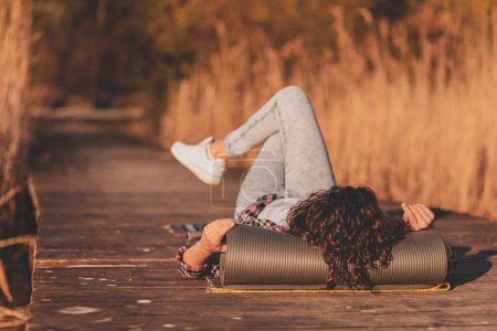 Téléchargez les photos : Femme allongée sur les quais du lac, relaxante après une longue journée de randonnée, profitant d'une belle journée d'automne dans la nature - en image libre de droit