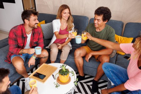 Foto de Vista de alto ángulo del grupo de amigos que se divierten pasando tiempo libre juntos en casa, sentados en el sofá, tomando café y jugo y haciendo un brindis - Imagen libre de derechos