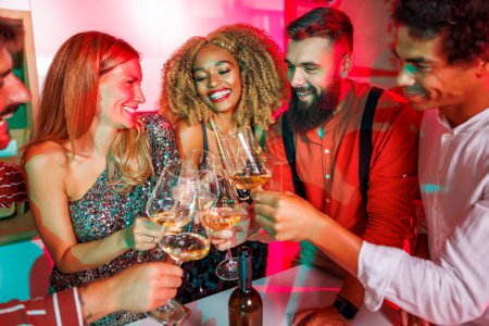 Foto de Grupo de jóvenes amigos alegres divirtiéndose en la fiesta de la casa, haciendo un brindis levantando copas de vino, bailando y bebiendo - Imagen libre de derechos