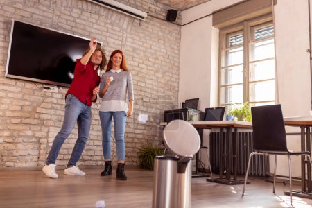 Photo for Business colleagues having fun at the office, playing trash can basketball; freelancers working in coworking space, taking a break and having fun - Royalty Free Image